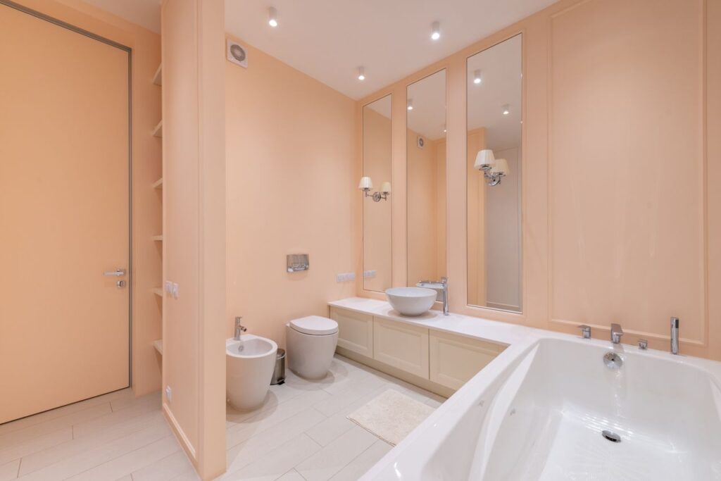 Interior of spacious bathroom with beige walls and clean white bath and sink placed near toilet and bidet